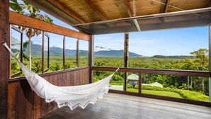 A wooden deck with a hammock, large windows, and a view of a lush landscape. - Daintree Holiday Homes - La Vista - Private Pool & Jet Spa - Ocean Views (Cow Bay)