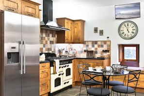 A kitchen with wooden cabinets, a stainless steel refrigerator, a stove, and a dining table with chairs.