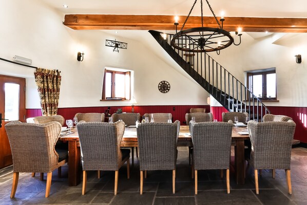 A dining area with wicker chairs, a wooden table, and a spiral staircase.