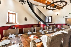 A dining area with wicker furniture, a wooden table set for a meal, and a staircase with a wheel chair.