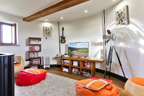 Un salon confortable avec une télévision, des étagères à livres, une guitare, des fauteuils en forme de poire et une fenêtre.