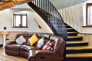 A brown leather sofa with multiple cushions, a wooden staircase with black railings, and a window with a decorative item.