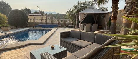 Ein Poolbereich mit Liegestuhl, Tisch und einer Pergola.