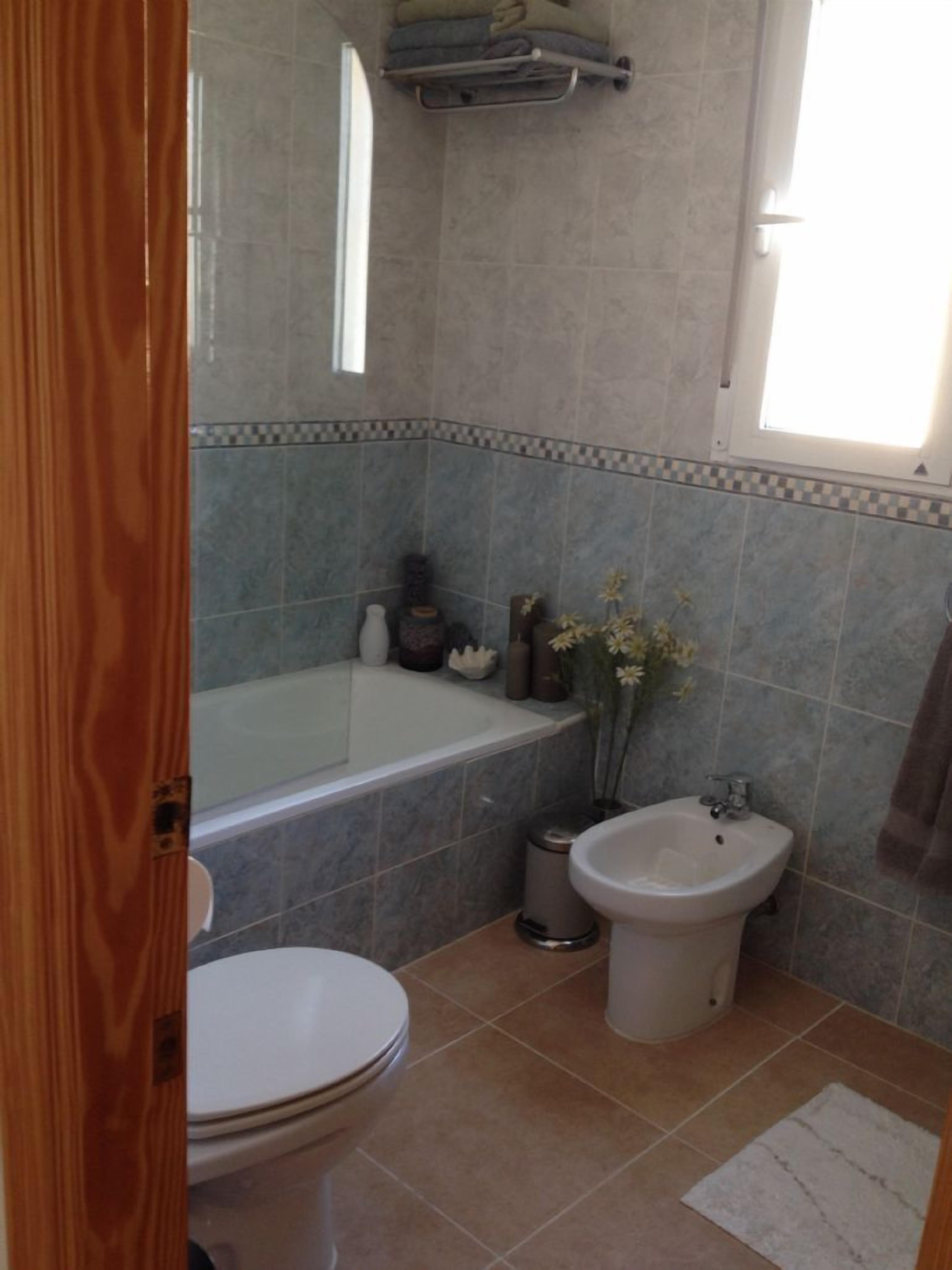 A bathroom with a bathtub, toilet, bidet, and a small window.
