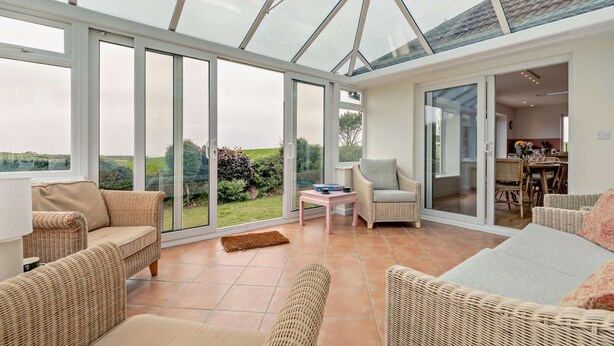 A spacious conservatory with large glass doors, wicker furniture, and a view of the outdoors.