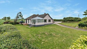 A single-story house with a conservatory, surrounded by a well-maintained lawn and a paved driveway.