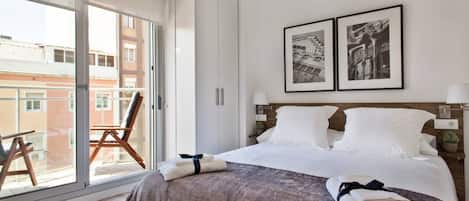A hotel room with a bed, a chair, a balcony, and two framed pictures on the wall.