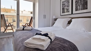 Une chambre d’hôtel avec un grand lit, une chaise près de la fenêtre et deux tableaux encadrés au mur.
