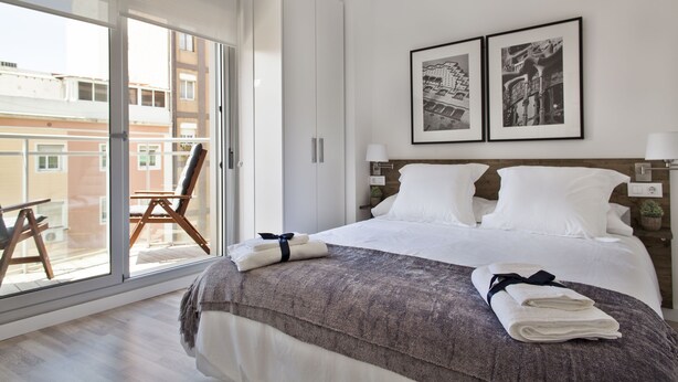 Une chambre d’hôtel avec un grand lit, une vue à travers une porte coulissante, un fauteuil près de la fenêtre et deux tableaux encadrés au mur.