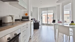 Une cuisine moderne dotée d’un plan de travail en bois, d’appareils électroménagers intégrés et d’un coin repas avec une table en verre et des chaises blanches.