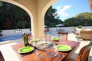 An outdoor dining area with a pool view, a wooden table set with green plates, and wicker furniture. - Finca Nora, Altea, Altea (Altea)