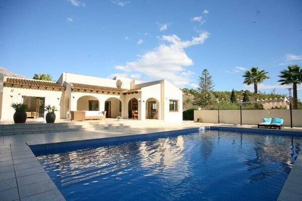 A poolside area with a swimming pool, a building with a tiled roof, and palm trees in the background. - Finca Nora, Altea, Altea (Altea)