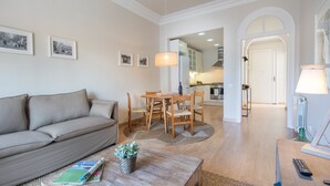 A living room with a sofa, a wooden coffee table with a plant, a dining table with chairs, and a kitchen in the background. - Bailen Terrace - Habitat Apartments (Barcelona)