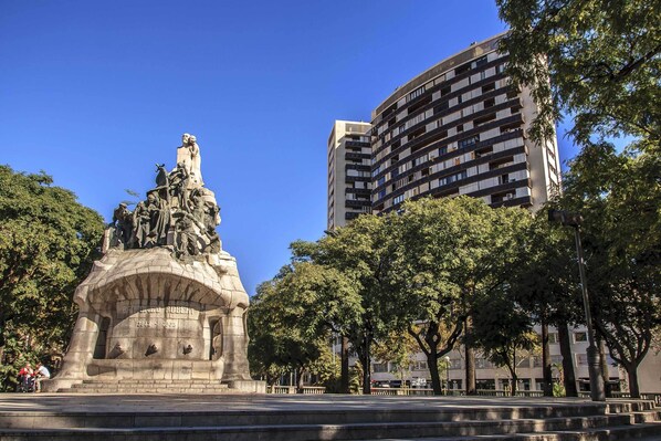 A statue in a park with a modern building in the background.