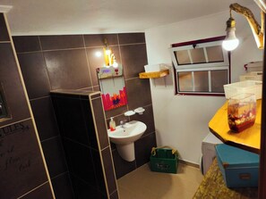 A bathroom with a toilet, sink, and a mirror. There is a window above the sink and a shelf with a bottle. - under the bridge :) . (praia da vitoria)