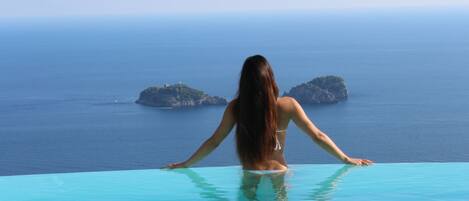 A person standing at the edge of an infinity pool with a view of the sea and islands.