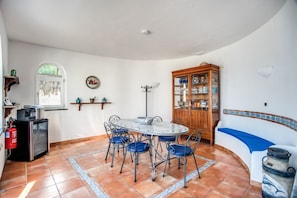 Zona pranzo con tavolo rotondo, sedie, mobiletto con vetrine, divano ed estintore.