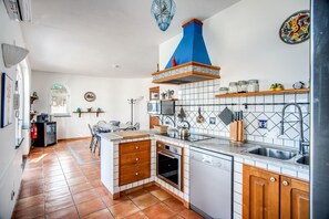 Eine Küche mit weiß gefliestem Fliesenspiegel, Holzschränken, einer blauen Dunstabzugshaube und einem Fliesenboden.