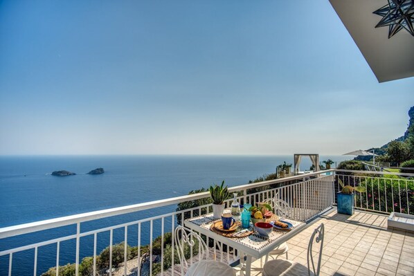 Un balcone con un tavolo apparecchiato per mangiare, con vista sulla costa, sul mare e su isole in lontananza.