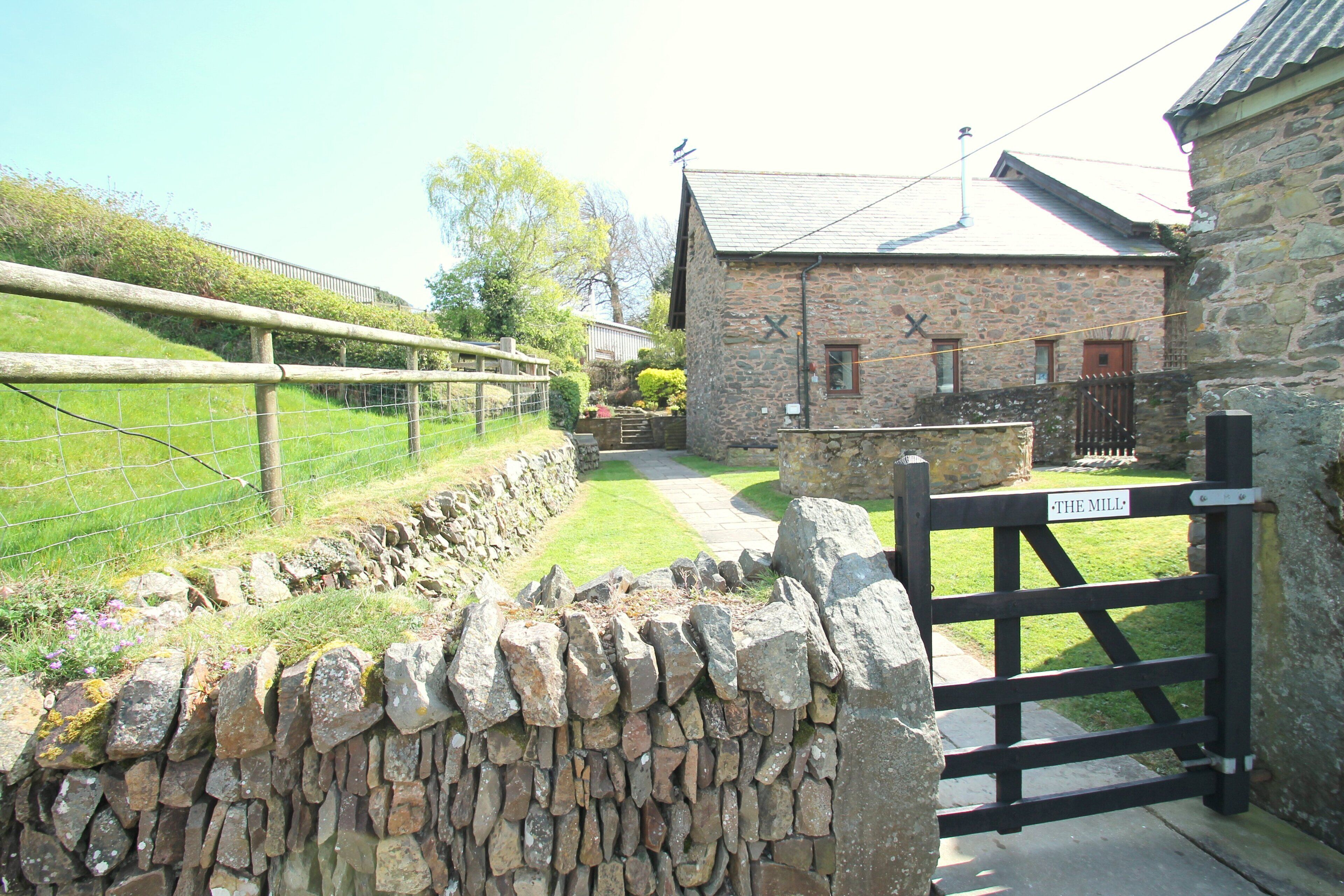 A stone building with a sign reading 'The Mill,' a stone wall, and a wooden gate.