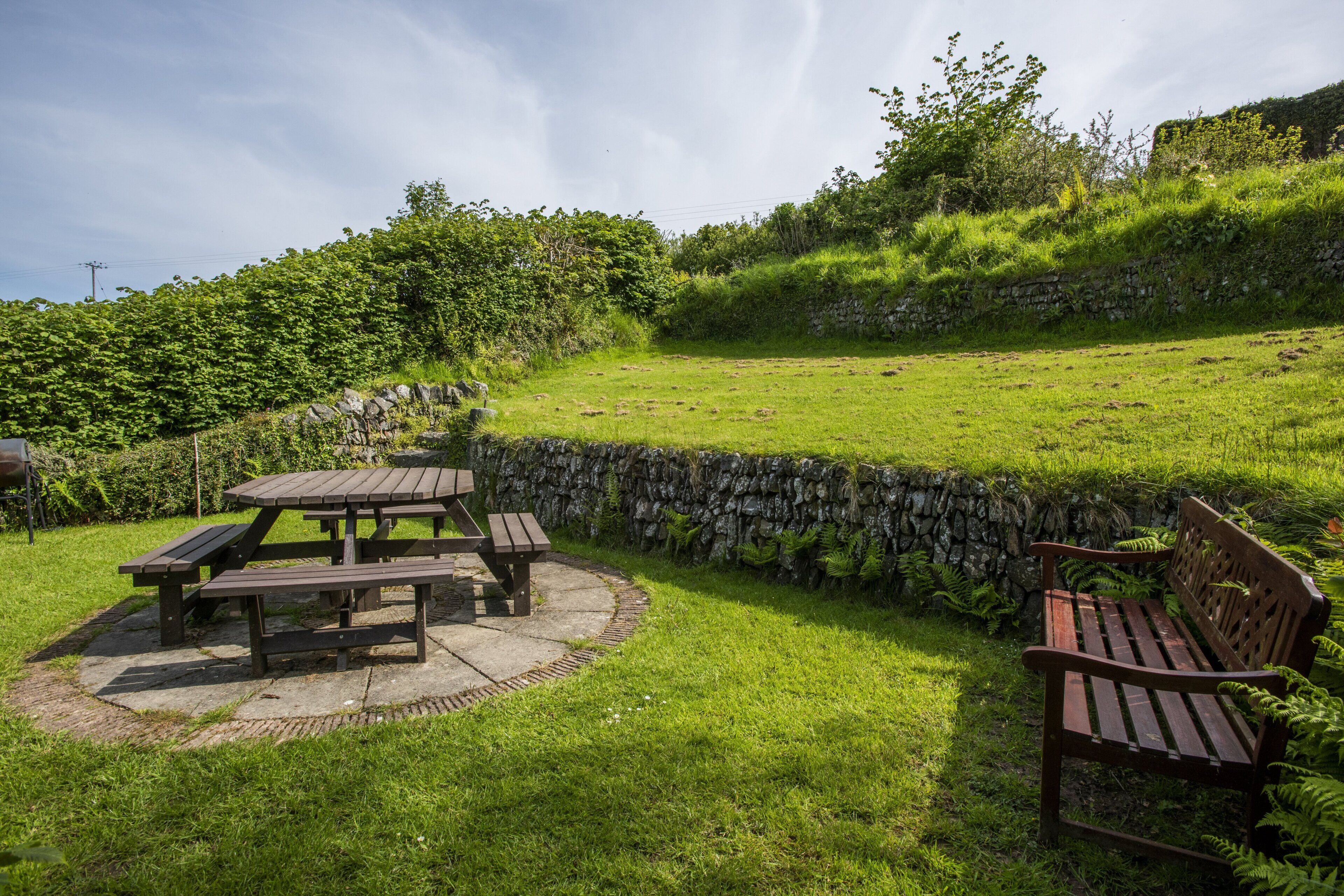 A picnic area with a stone wall, benches, and a grassy field.