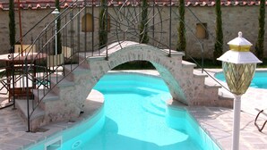 Una piscina con un puente de piedra, escalones y un farol.