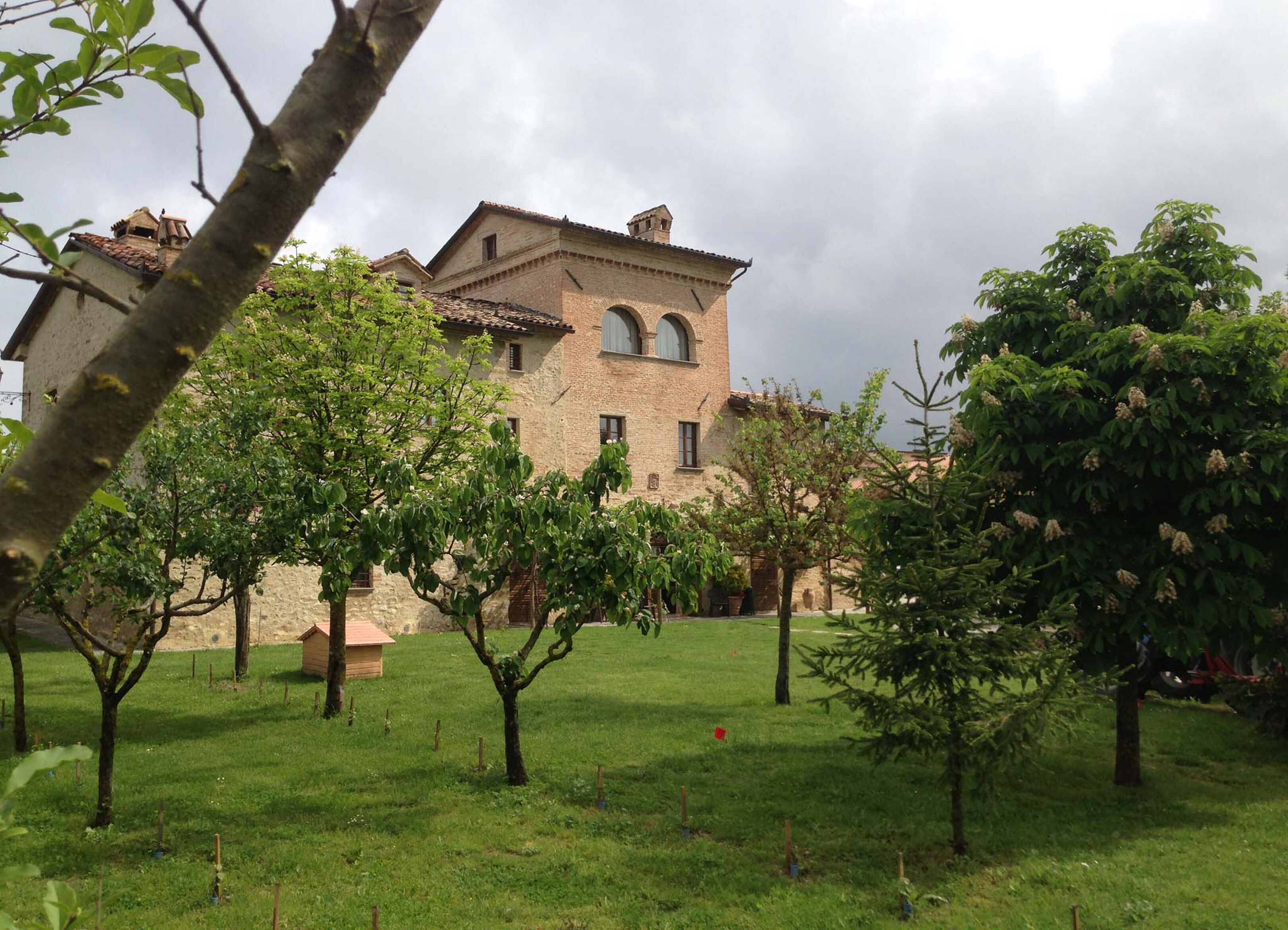 A stone building with a tiled roof, surrounded by a grassy area with trees.