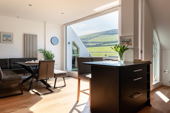 A modern living room with a dining area, large windows, and a view of the countryside.