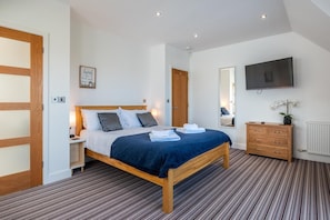 A modern bedroom with a wooden bed, a nightstand, a dresser, a mirror, and a flat-screen TV.