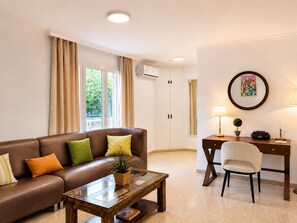 A furnished living room with a leather sofa, a glass-top coffee table, a desk with a chair, and a window with curtains. - AMELIE Villa piscina privada, BBQ y Wifi gratis (Miami Playa)