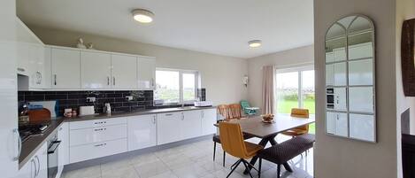 A modern kitchen with white cabinets, a dining area with a table and chairs, and a large window providing a view of the outdoors.