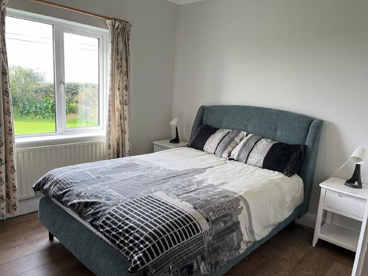 A bedroom with a bed, two bedside tables, a window with curtains, and a radiator.