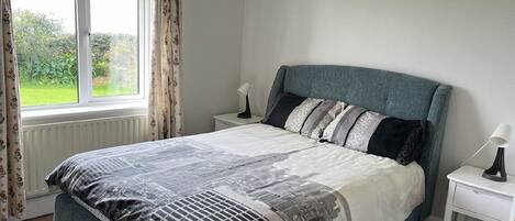 A bedroom with a bed, two bedside tables, a window with curtains, and a radiator.