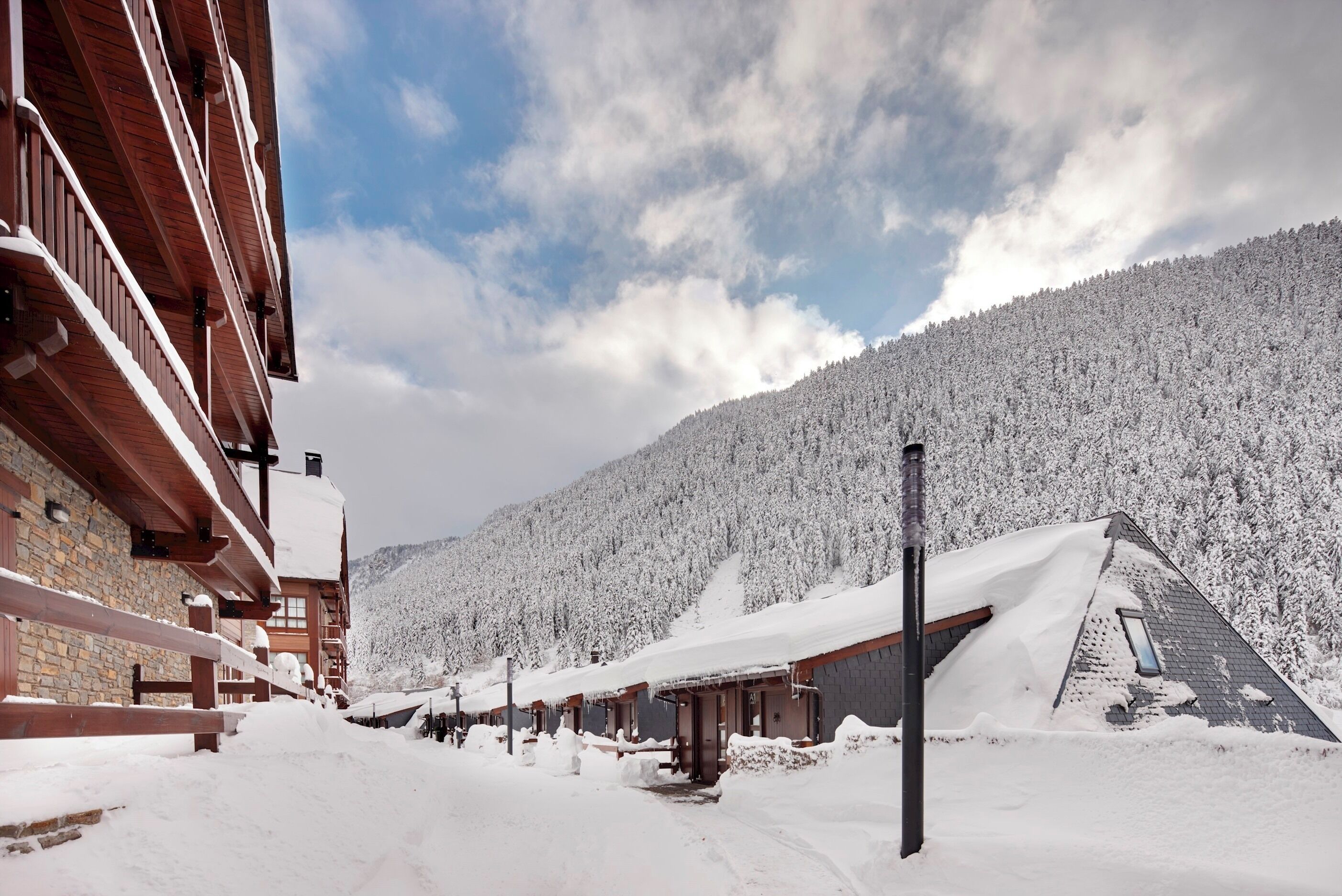 Un lodge imbiancato dalla neve, con facciata in legno, un muro in pietra e le montagne sullo sfondo.