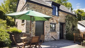 A stone building with a tiled patio, a green umbrella, and wooden furniture. - Four star cottage in glorious Devon countryside, indoor pool, sauna, WiFi (Tiverton)