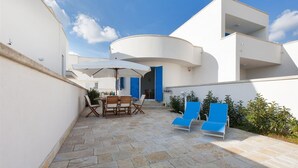 A courtyard with a table and chairs, a blue umbrella, and a blue door.