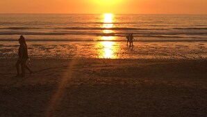 Strandszene bei Sonnenuntergang, mit Silhouetten von Personen und einem klaren Himmel.