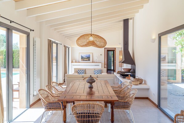 A dining area with a wooden table and wicker chairs, a sofa with patterned cushions, and a hanging light fixture.