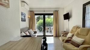 A room with a sofa, armchairs, a table, a TV, and a sliding glass door leading to an outdoor area with a table and chairs.