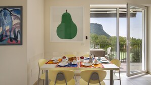 A dining area with a table set for four, chairs, a painting, and a large window with a mountain view. - Cà Gardesana With Pool (Garda)