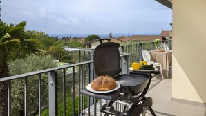 A balcony with a grill, a loaf of bread, and a table with a chair. - Cà Gardesana With Pool (Garda)
