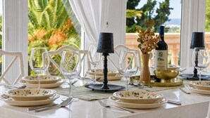 Een eettafel gedekt met borden, glazen, bestek en een fles wijn, met uitzicht op palmbomen en een balkon.