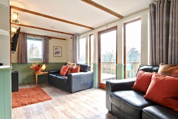 Ein geräumiges Wohnzimmer mit einer Couch, einem Couchtisch und einem Kamin. Große Fenster sorgen für natürliches Licht und einen Blick ins Freie.