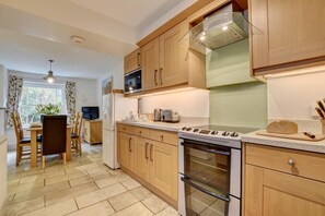 Une cuisine moderne avec des meubles en bois, un four encastré, un four à micro-ondes et un coin repas comprenant une table et des chaises.