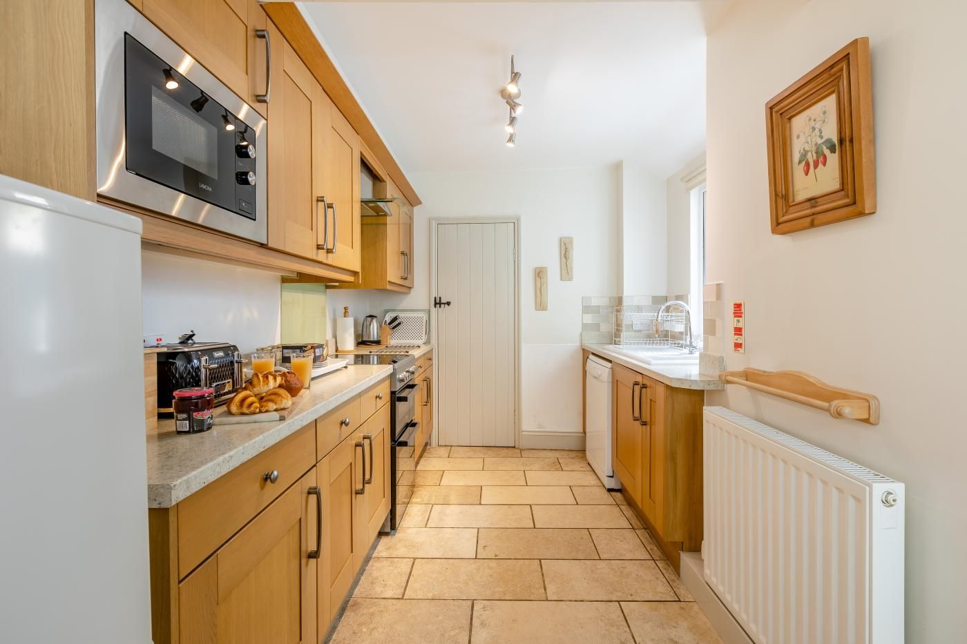 A narrow kitchen with wooden cabinets, a stainless steel microwave, and a white door.