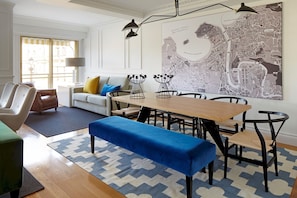 Una sala de estar moderna con comedor, que presenta un mapa grande en la pared, un sofá con cojines, una mesa de centro y un banco.