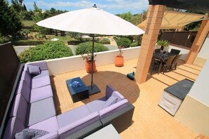 Un patio con un sofá, una mesa, una sombrilla y una planta en maceta.