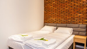 Une chambre d’hôtel moderne avec une tête de lit décorée d’un motif en briques, un lit soigneusement fait avec du linge de lit blanc, et deux tables de chevet.