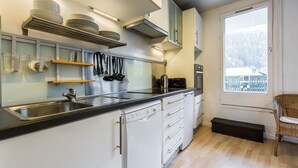Een moderne keuken met witte kasten, roestvrijstalen apparatuur en een groot raam met uitzicht op een besneeuwd landschap.