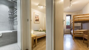 Een moderne hotelkamer met een douche, een bed met een groene deken, een houten stapelbed en een ingelijst beeld aan de muur.